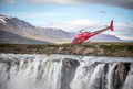 Helicopter flying above a waterfall and Icelandic mountains, highlighting the incredible scenery featured in FlyOver Iceland and sightseeing