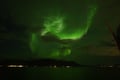 Bright green Northern Lights stretching across the night sky above the sea