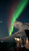 Green Northern Lights glowing through the clouds over the ocean near Reykjavík, Iceland.