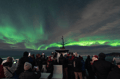 Guests gathered on deck beneath vivid green Northern Lights during an aurora cruise from Reykjavík.