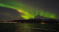 Green Aurora Borealis illuminating the sky and coastline during a Northern Lights boat tour.