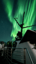 Bright green Northern Lights above a boat during an aurora cruise from Reykjavík, Iceland.